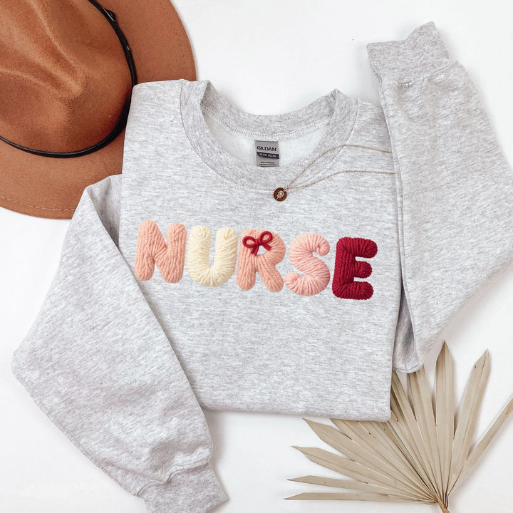 Gray sweatshirt with 'NURSE' embroidered in colorful letters, faux yarn style on a white background.