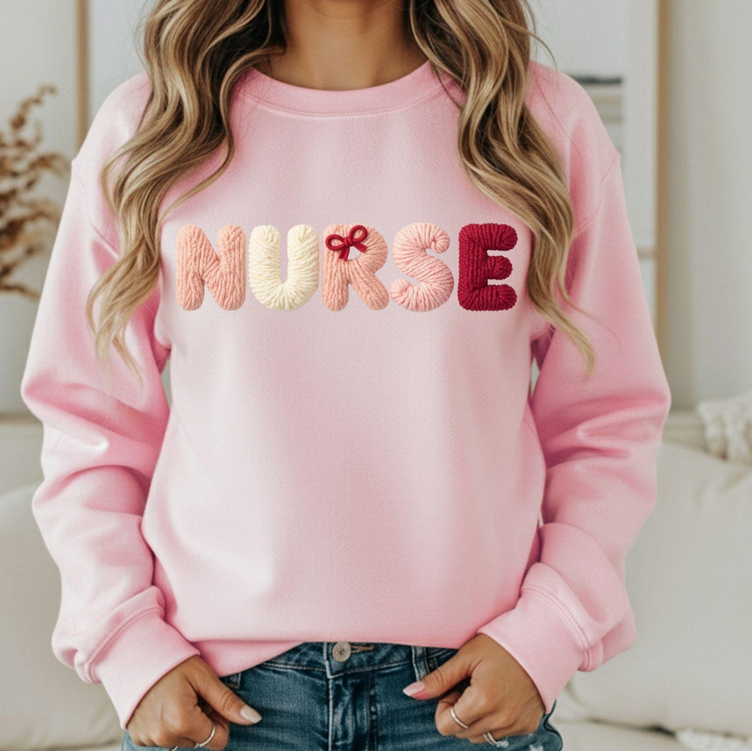 Pink sweatshirt with 'NURSE' embroidered in colorful letters, a faux yarn style, worn by a person
