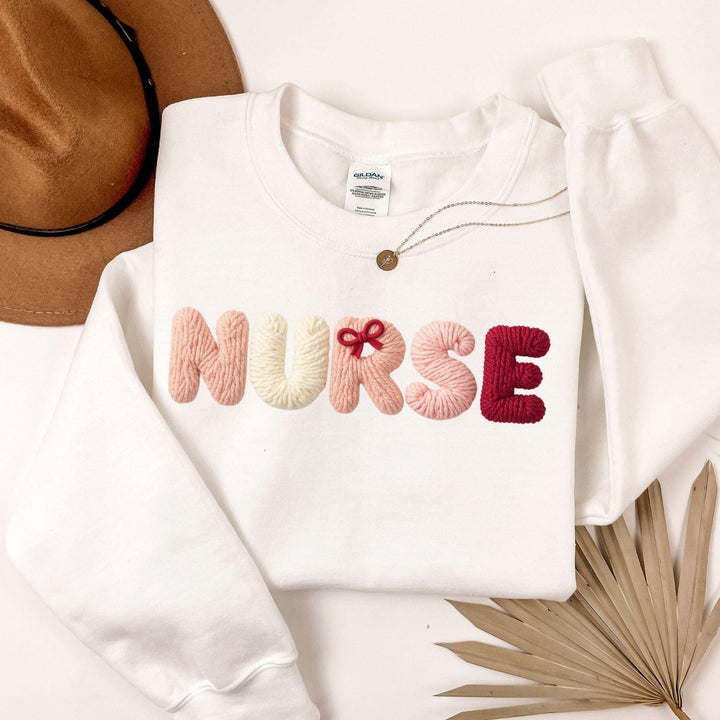 White sweatshirt with 'NURSE' text in colorful letters, faux yarn style on a neutral background