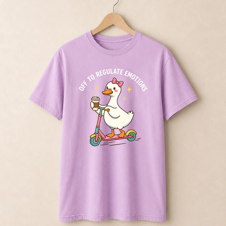 Purple t-shirt with a cartoon duck on a scooter and text, hanging on a beige wall.